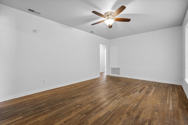 spare room featuring baseboards, visible vents, a ceiling fan, and dark wood-style floors