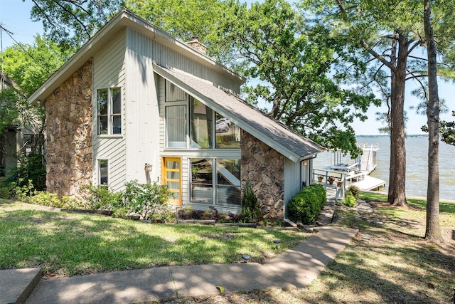 view of front of house featuring a front lawn, stone siding, a water view, and a chimney