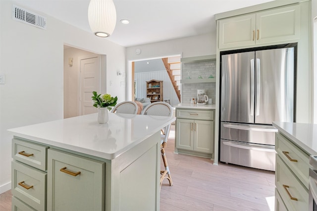 kitchen with green cabinets, light countertops, backsplash, visible vents, and freestanding refrigerator