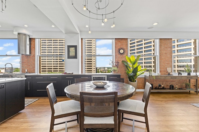 dining room with light wood-type flooring, a healthy amount of sunlight, and brick wall