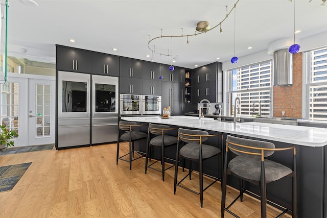 kitchen with built in refrigerator, stainless steel oven, light wood-style flooring, and dark cabinetry