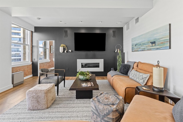 living area with baseboards, wood finished floors, visible vents, and a glass covered fireplace