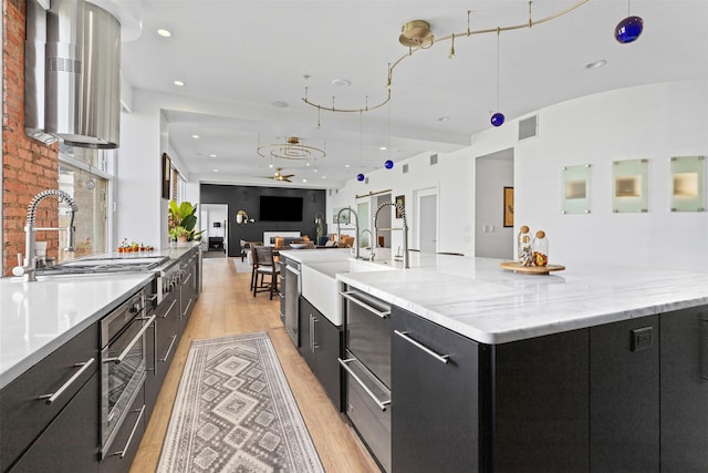 kitchen with a large island with sink, a sink, light wood-type flooring, visible vents, and dark cabinets