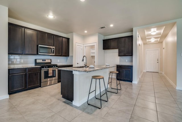 kitchen featuring a sink, stainless steel appliances, tasteful backsplash, visible vents, and light stone counters