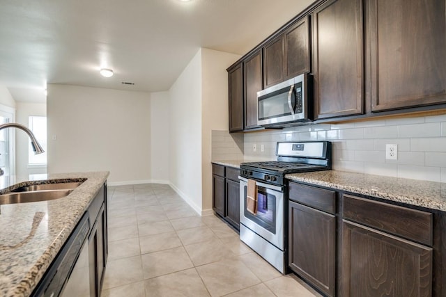 kitchen with a sink, appliances with stainless steel finishes, decorative backsplash, light stone counters, and dark brown cabinets