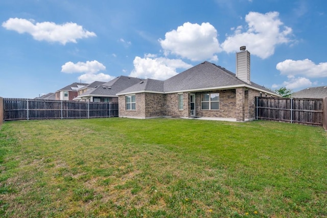 back of house with a chimney, brick siding, a fenced backyard, and a lawn