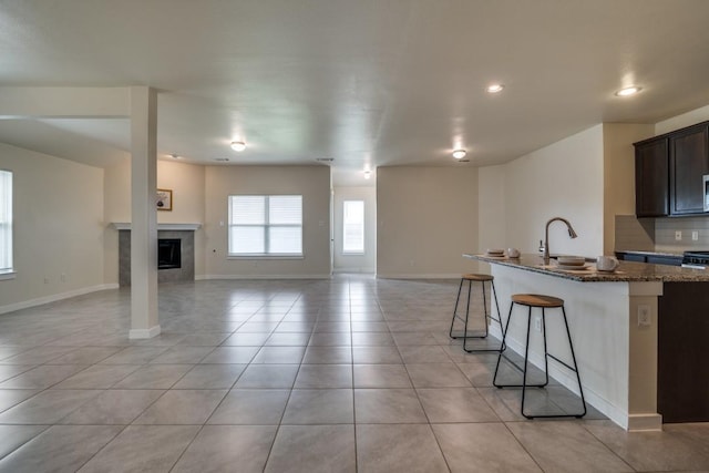 kitchen with a sink, light tile patterned flooring, dark stone countertops, open floor plan, and an island with sink