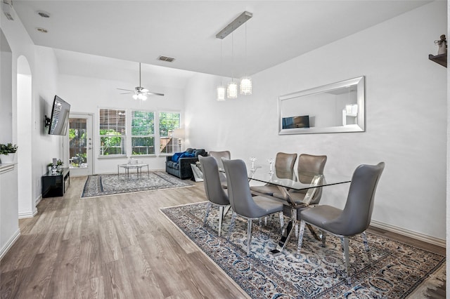 dining space featuring arched walkways, visible vents, baseboards, a ceiling fan, and wood finished floors