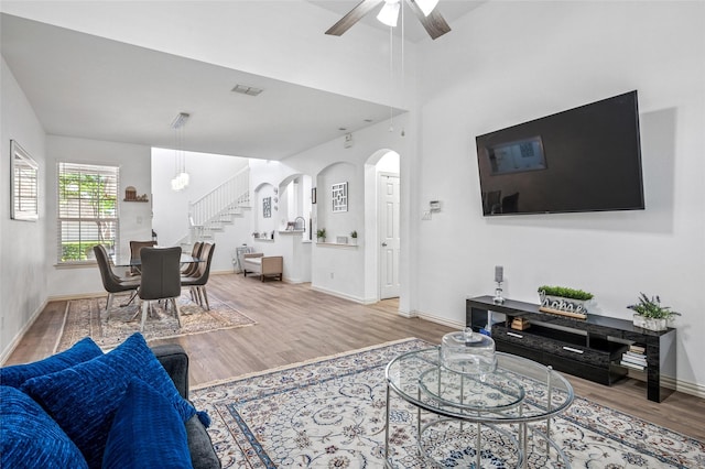 living room with wood finished floors, visible vents, arched walkways, stairs, and ceiling fan