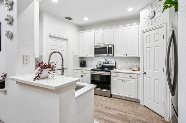 kitchen featuring stainless steel appliances, a peninsula, visible vents, backsplash, and white cabinetry