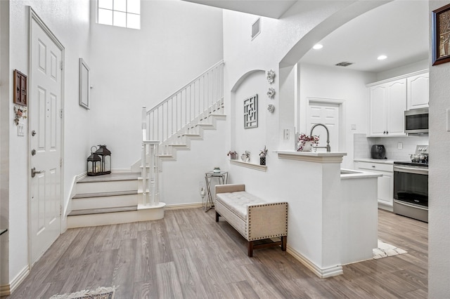 kitchen with arched walkways, white cabinetry, light wood-style floors, light countertops, and appliances with stainless steel finishes