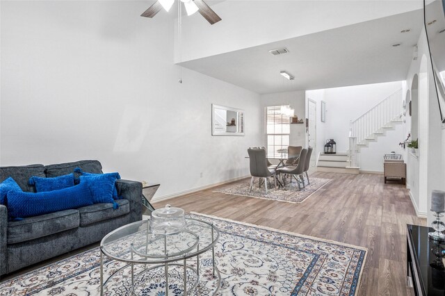 living area with ceiling fan, wood finished floors, visible vents, and stairway