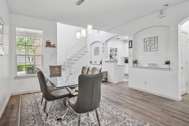 dining space with arched walkways, baseboards, recessed lighting, wood finished floors, and stairs