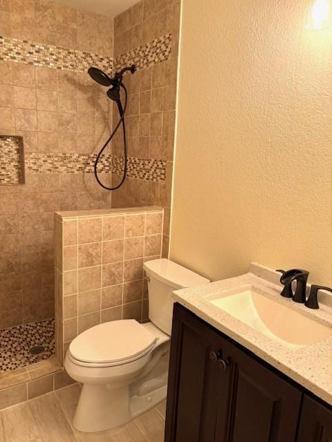 bathroom with a tile shower, toilet, and vanity
