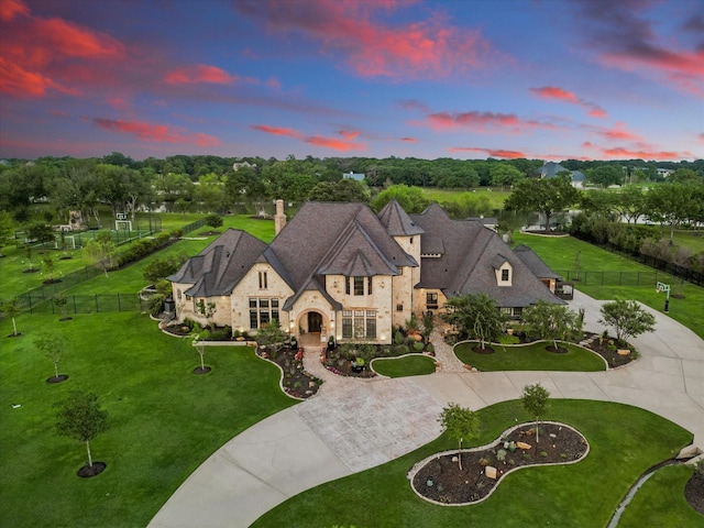 french country home featuring curved driveway, a chimney, fence, and stone siding