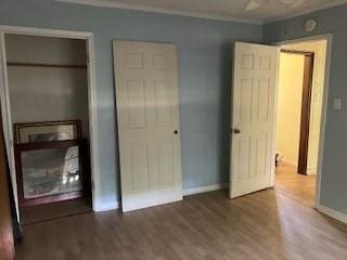 unfurnished bedroom featuring baseboards, wood finished floors, and crown molding