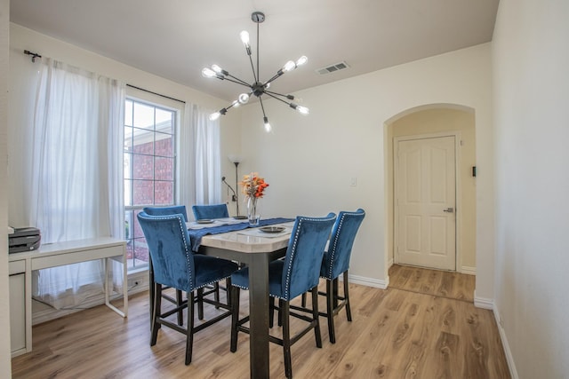 dining space with light wood finished floors, an inviting chandelier, visible vents, arched walkways, and baseboards
