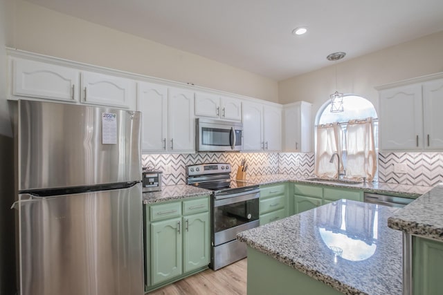 kitchen featuring light stone counters, a sink, green cabinets, stainless steel appliances, and white cabinetry