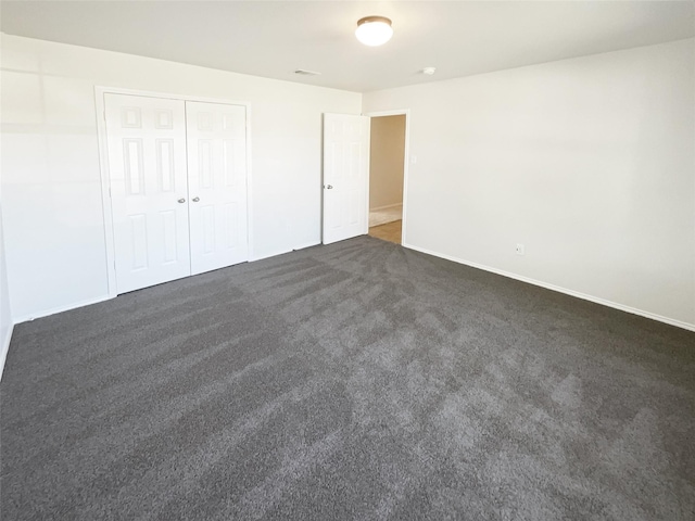 unfurnished bedroom with dark carpet and a closet