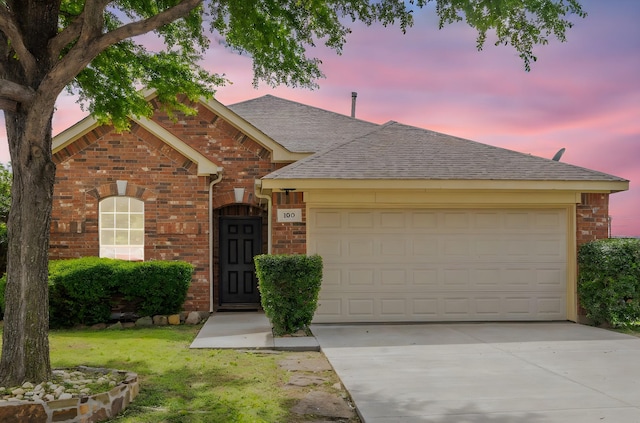 view of front of house featuring roof with shingles, driveway, brick siding, a garage, and a yard