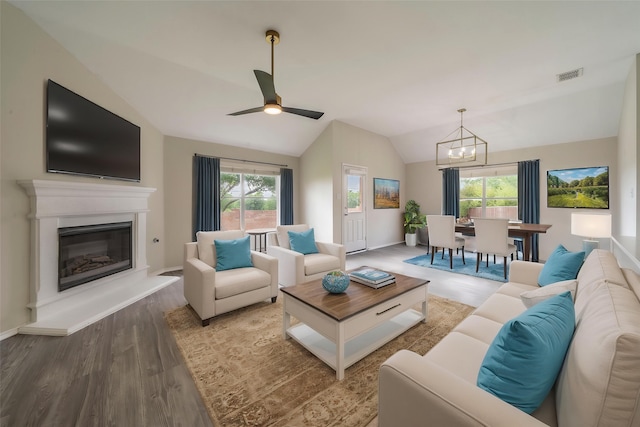 living room featuring wood finished floors, a glass covered fireplace, baseboards, lofted ceiling, and visible vents