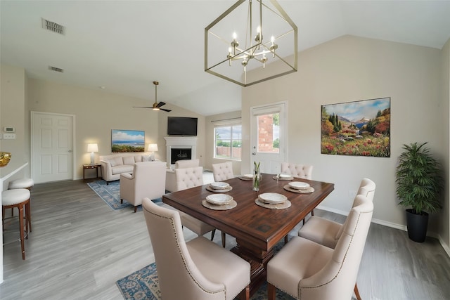 dining room featuring vaulted ceiling, visible vents, a fireplace, and light wood-style flooring