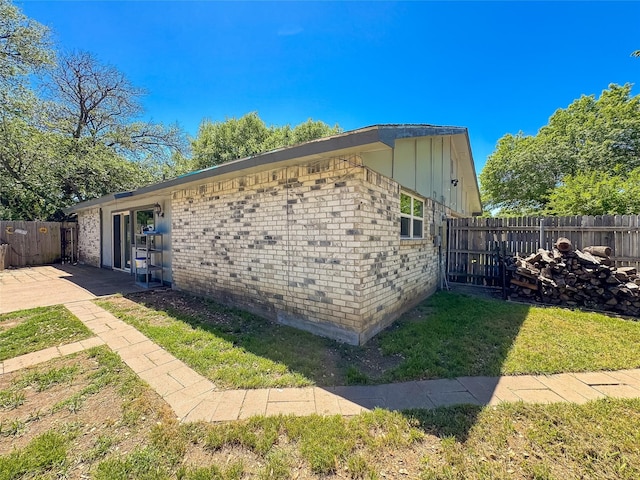 view of side of home featuring fence, a lawn, brick siding, and board and batten siding