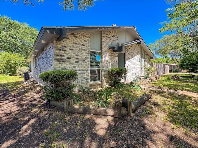 view of property exterior featuring central air condition unit, brick siding, and fence