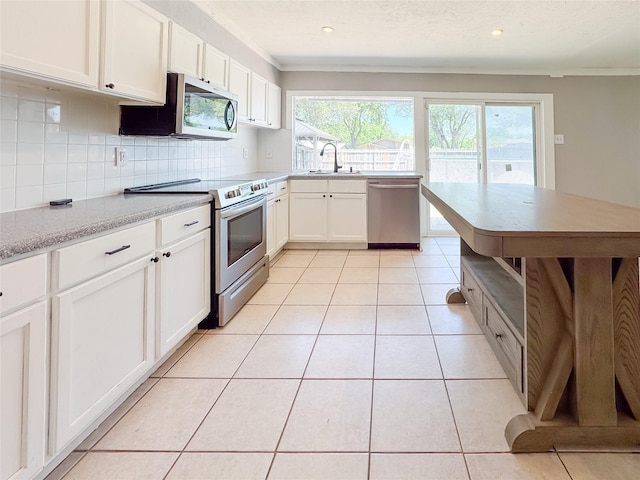 kitchen with a sink, decorative backsplash, light tile patterned floors, white cabinets, and appliances with stainless steel finishes