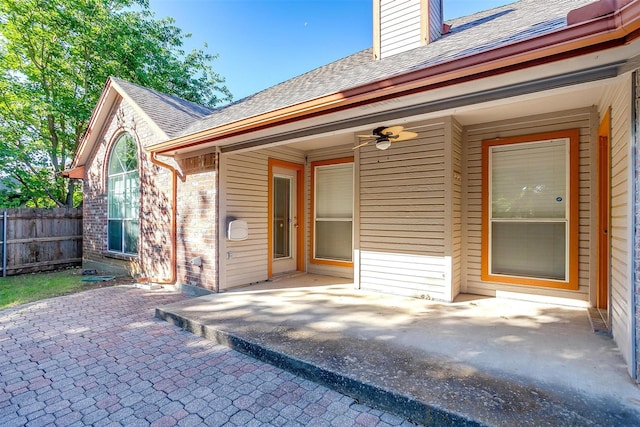 exterior space with brick siding, roof with shingles, fence, and a patio area
