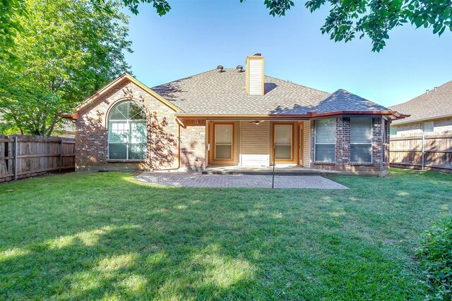 back of house featuring a chimney, a fenced backyard, a patio area, a lawn, and brick siding