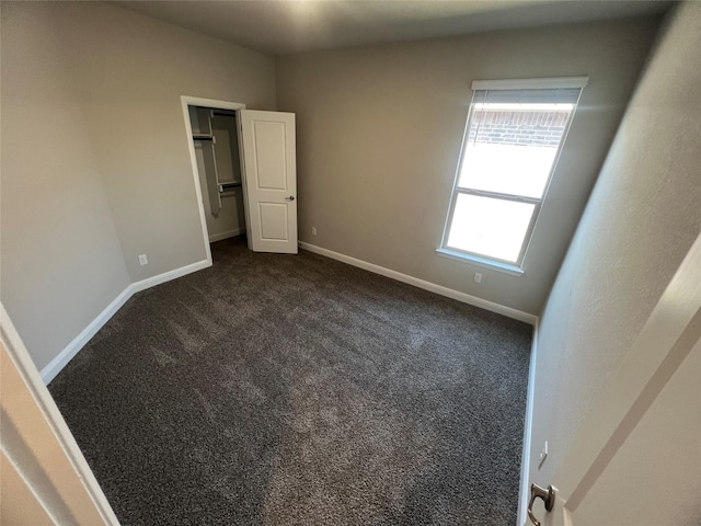 unfurnished bedroom with baseboards, dark carpet, and a walk in closet