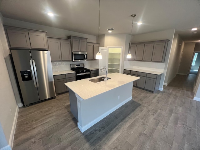 kitchen with an island with sink, wood finished floors, gray cabinets, a sink, and appliances with stainless steel finishes