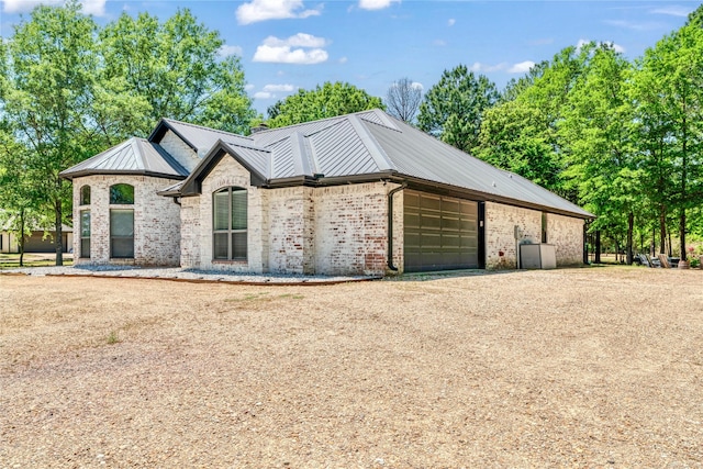 view of front facade with brick siding, driveway, a garage, and metal roof