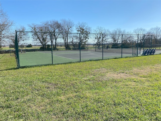 view of tennis court with a yard and fence
