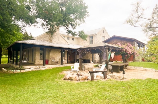 back of property with a gazebo, stone siding, a patio area, a lawn, and a fire pit