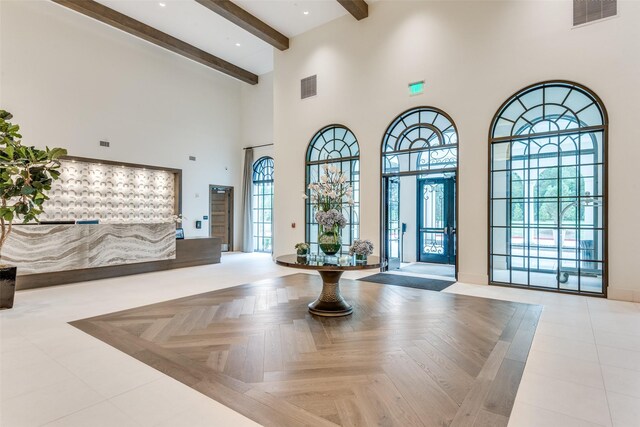 foyer entrance featuring visible vents, beam ceiling, and a high ceiling