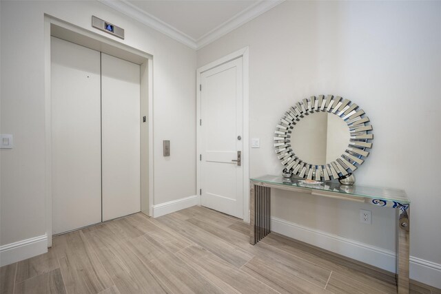 entryway with elevator, crown molding, baseboards, and light wood-style flooring