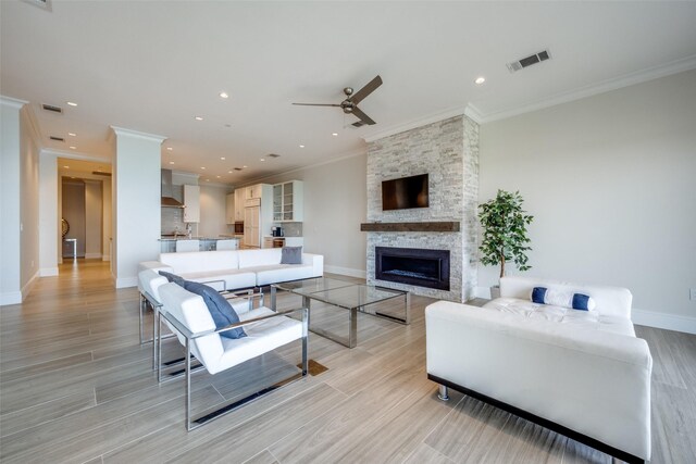 living room with a ceiling fan, crown molding, a fireplace, baseboards, and visible vents