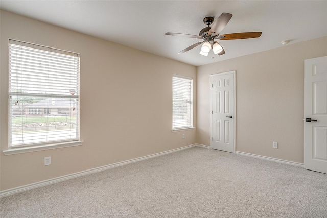 empty room featuring baseboards, ceiling fan, light colored carpet, and a wealth of natural light