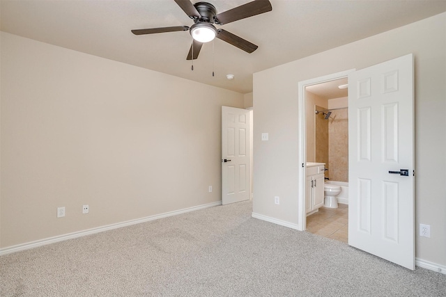 unfurnished bedroom featuring baseboards, ensuite bathroom, light carpet, and a ceiling fan