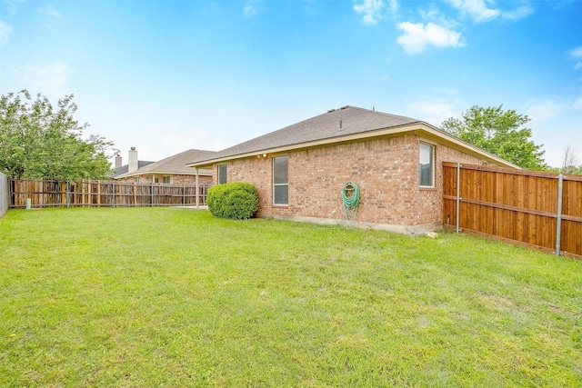 back of property with a fenced backyard, a yard, and brick siding