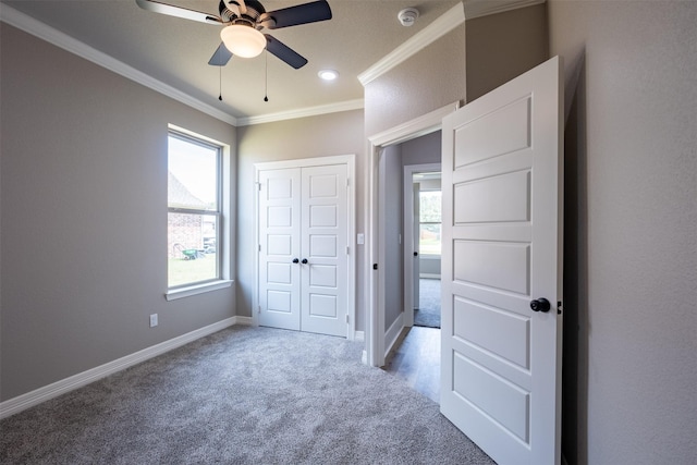 unfurnished bedroom featuring a closet, crown molding, baseboards, carpet flooring, and ceiling fan