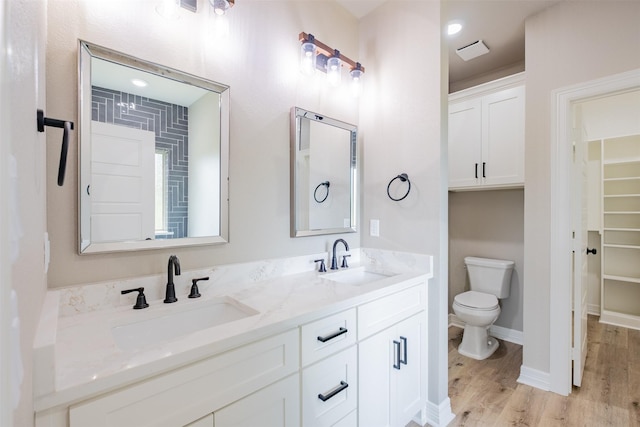bathroom with double vanity, wood finished floors, toilet, and a sink