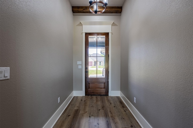 doorway with beamed ceiling, a textured wall, baseboards, and dark wood finished floors