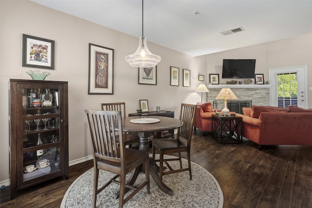 dining space with dark wood-style flooring, baseboards, visible vents, lofted ceiling, and a stone fireplace