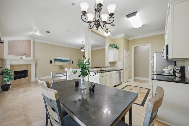 dining space featuring light tile patterned floors, a fireplace, ceiling fan with notable chandelier, and visible vents