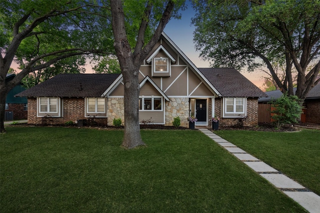 view of front of home featuring stucco siding, fence, stone siding, roof with shingles, and a front yard