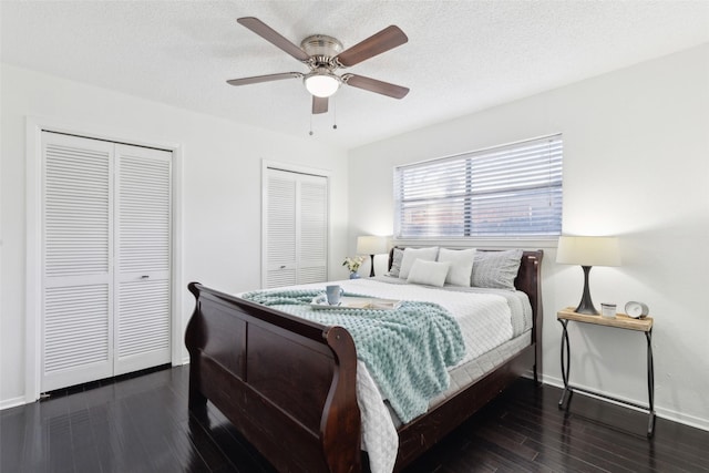 bedroom featuring a textured ceiling, baseboards, a ceiling fan, wood finished floors, and multiple closets