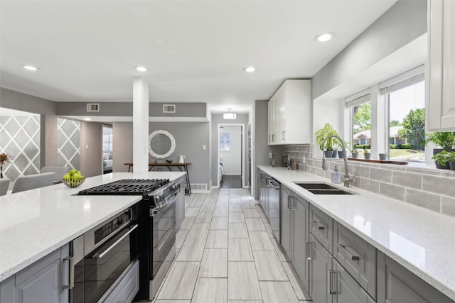 kitchen with a sink, gray cabinets, backsplash, black gas range, and visible vents